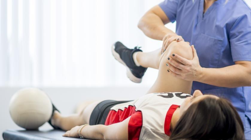 An urgent care provider checks a female athlete's knee injury 